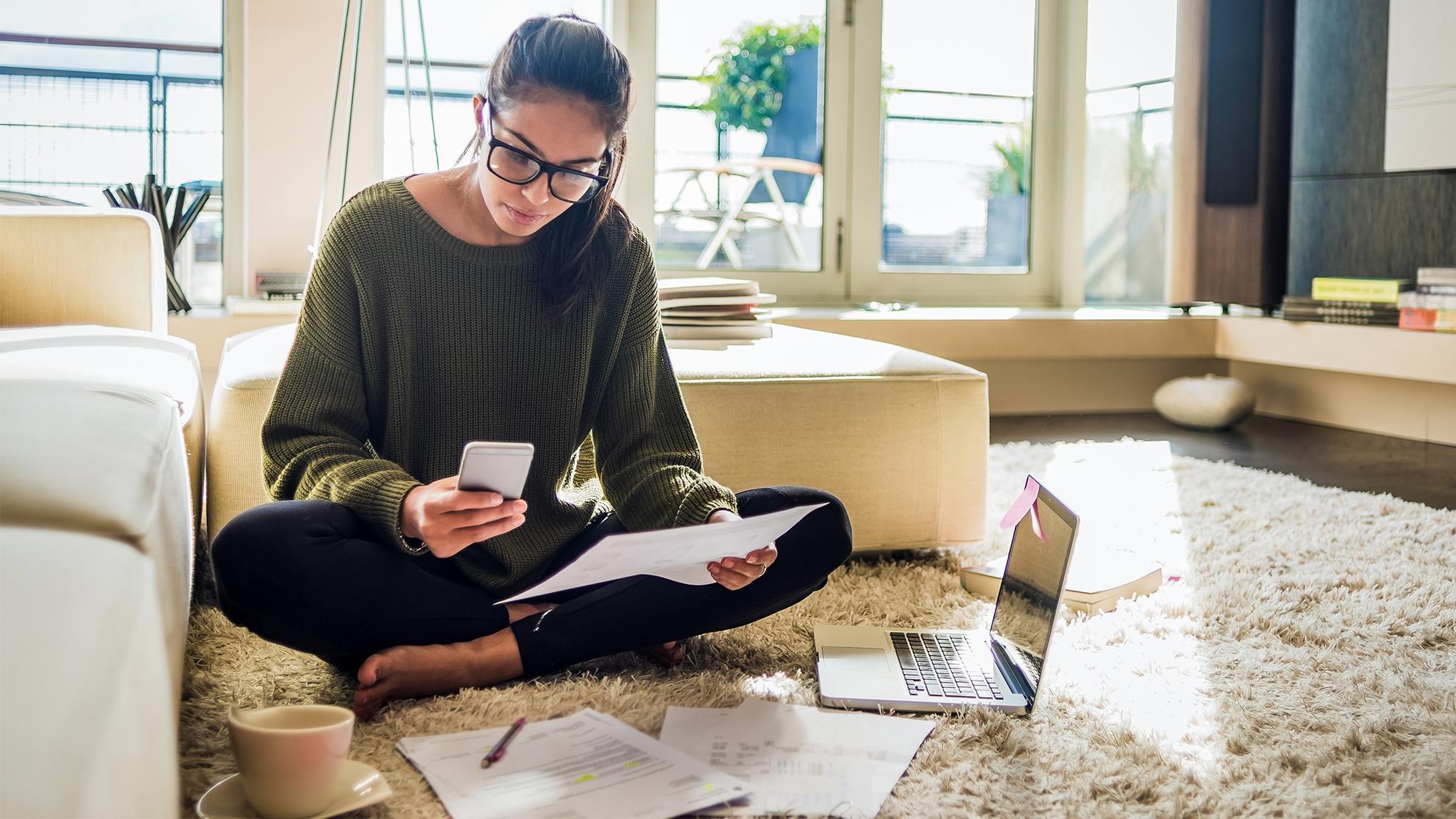 woman sitting on the floor with a laptop, paper and phone